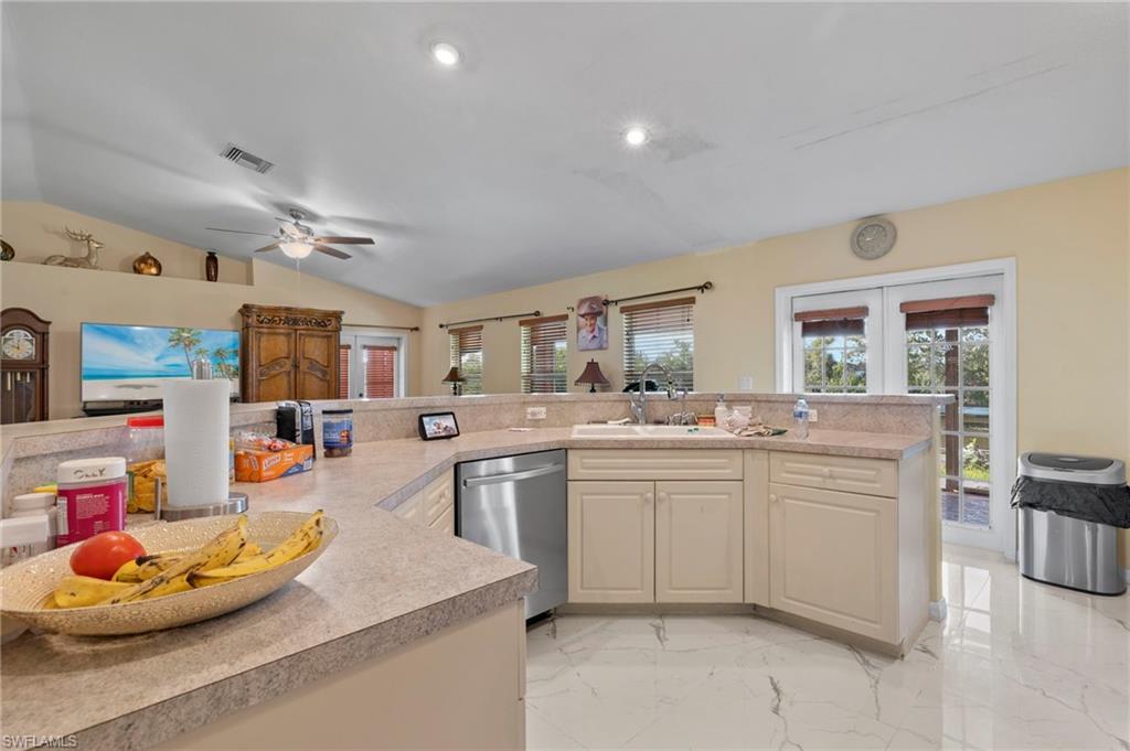 Spacious kitchen featuring a large wrap-around peninsula, stainless steel dishwasher, double basin sink, and ample cabinetry