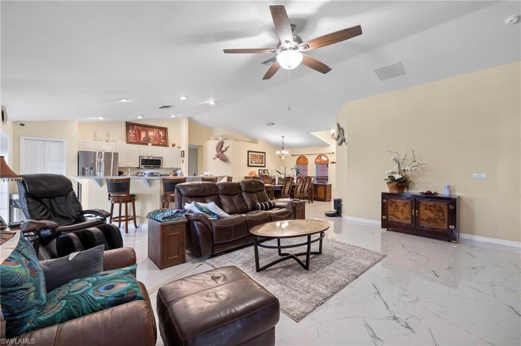 Spacious living area featuring vaulted ceilings, a ceiling fan, recessed lighting, and large format marble-look tile flooring