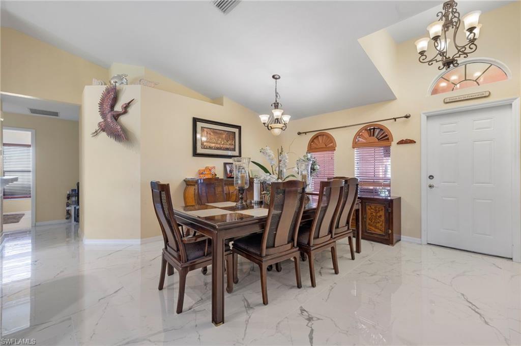 Vaulted ceiling dining area featuring marble-look tile flooring, a multi-paneled entry door with an arched transom, and two arched windows with wood blinds