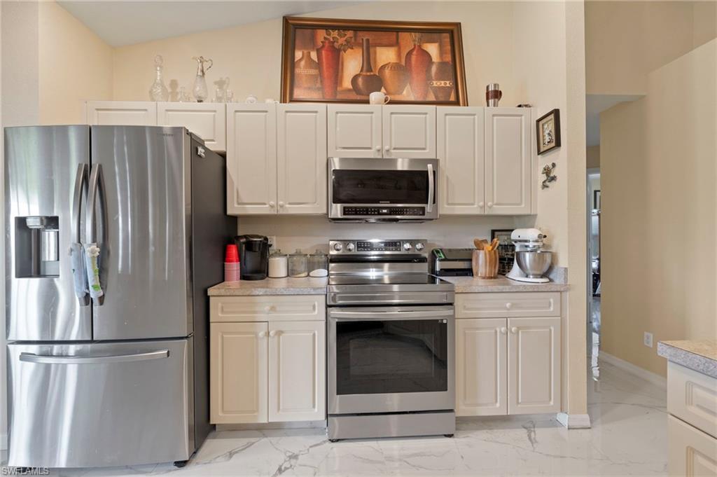 Kitchen featuring stainless steel appliances, light cabinetry, light countertops, and white tile flooring