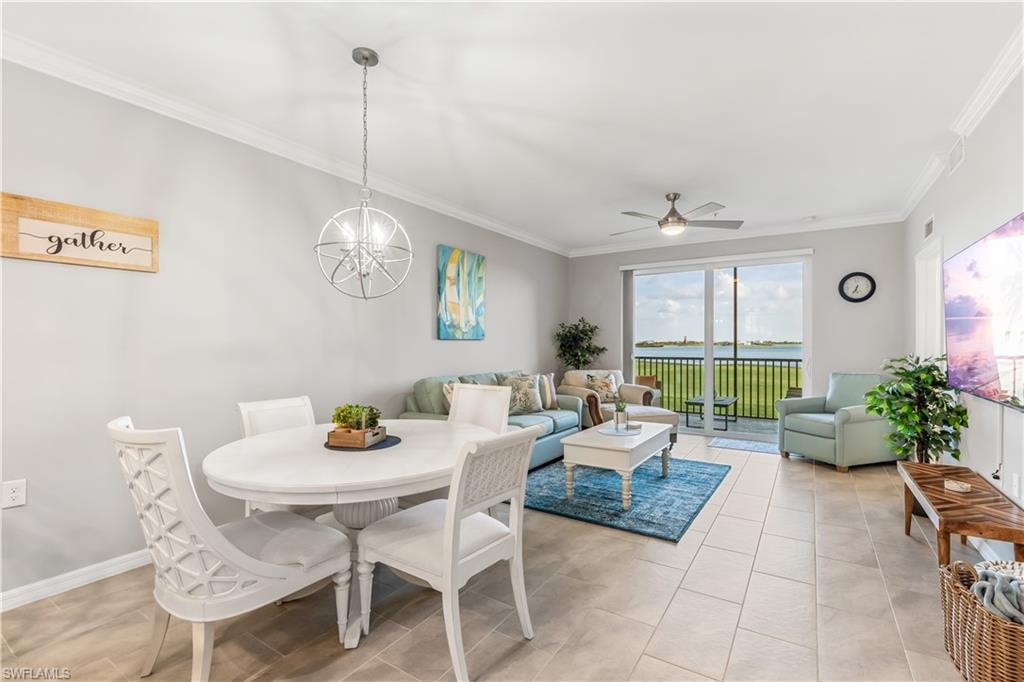 Dining area with ceiling fan with notable chandelier, crown molding, light tile flooring, and a water view