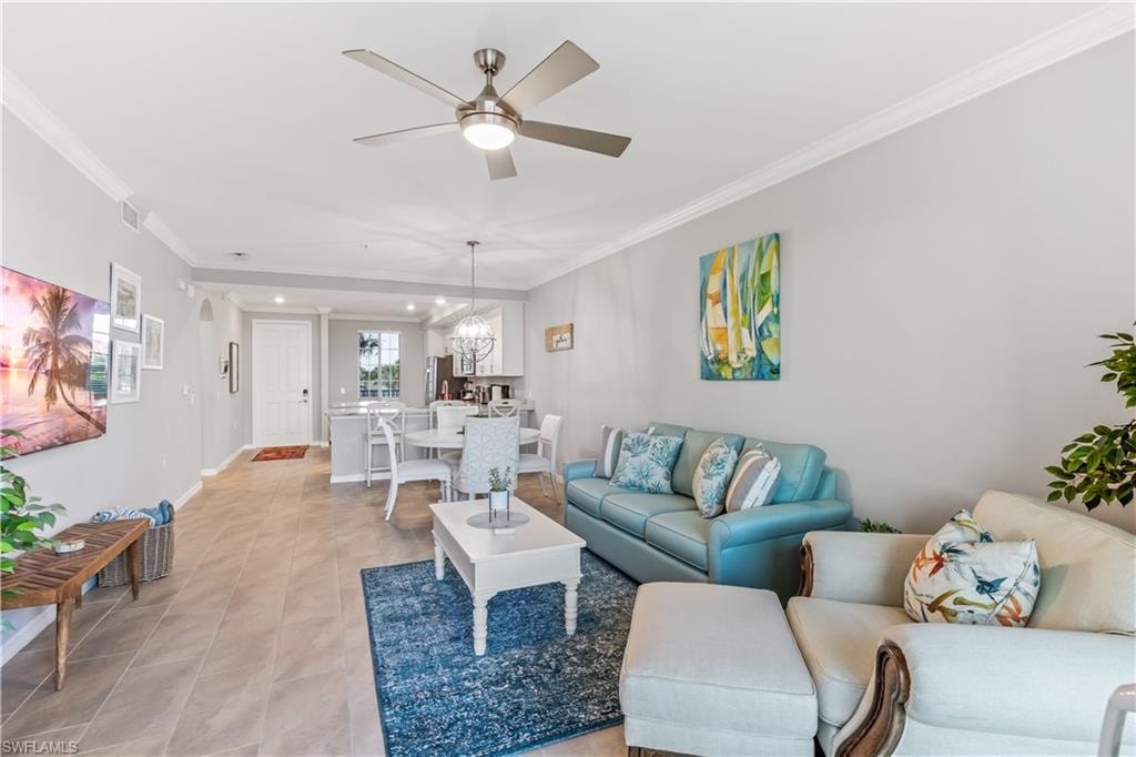 Tiled living room with crown molding and ceiling fan with notable chandelier