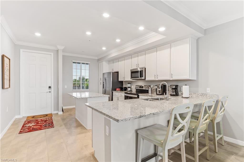 Kitchen with crown molding, stainless steel appliances, a breakfast bar area, kitchen peninsula, and sink
