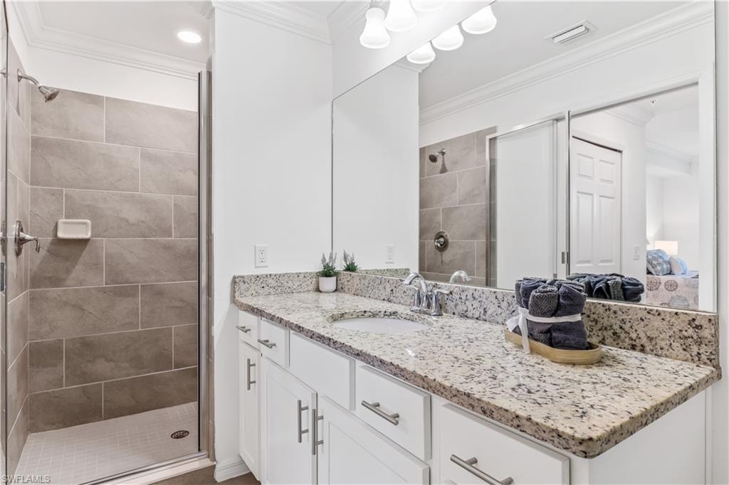 Bathroom with a shower with shower door, crown molding, and vanity