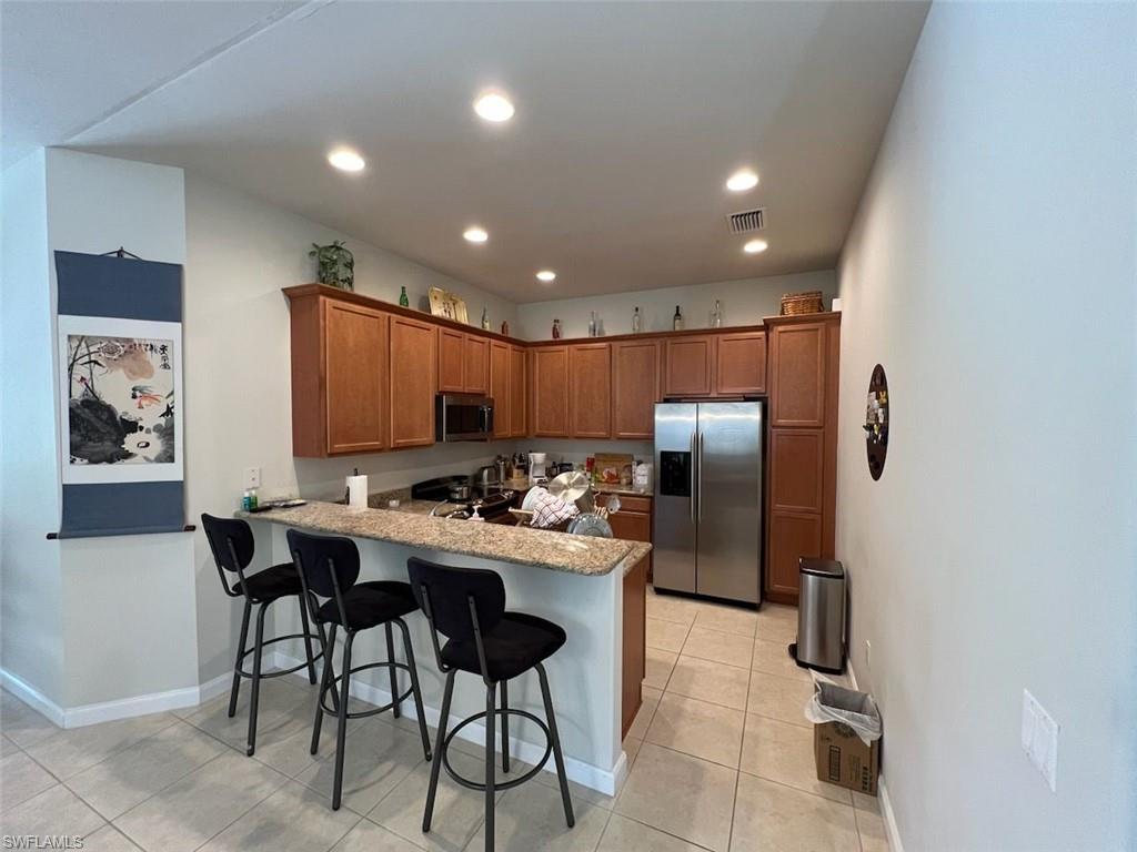 Kitchen with light tile patterned flooring, appliances with stainless steel finishes, kitchen peninsula, and a breakfast bar