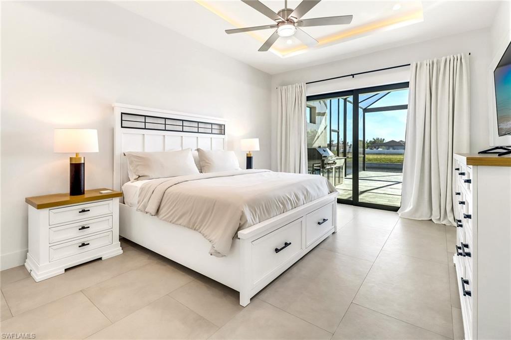 Spacious room featuring large format tile flooring, a tray ceiling with integrated lighting, a ceiling fan, and sliding glass doors opening to a screened outdoor area