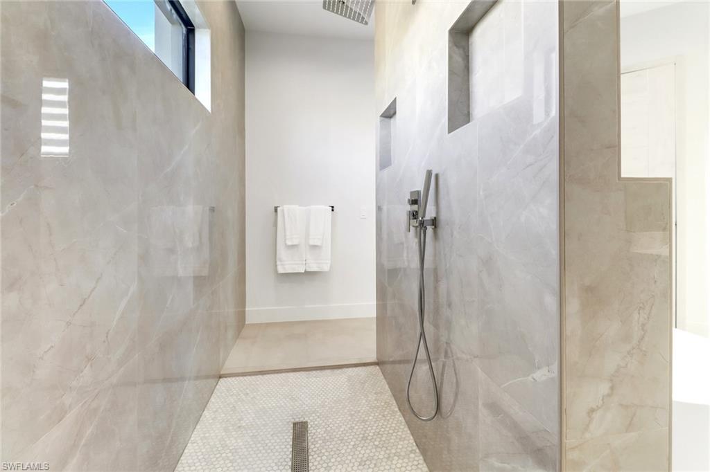 Walk-through shower featuring large format veined wall tiles, a mosaic tile floor, and a linear drain