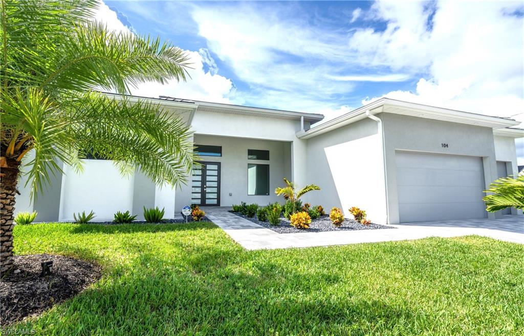 Modern stucco exterior featuring a dark paneled entry door with sidelights, a paver walkway, mature palm trees, and a two-car garage