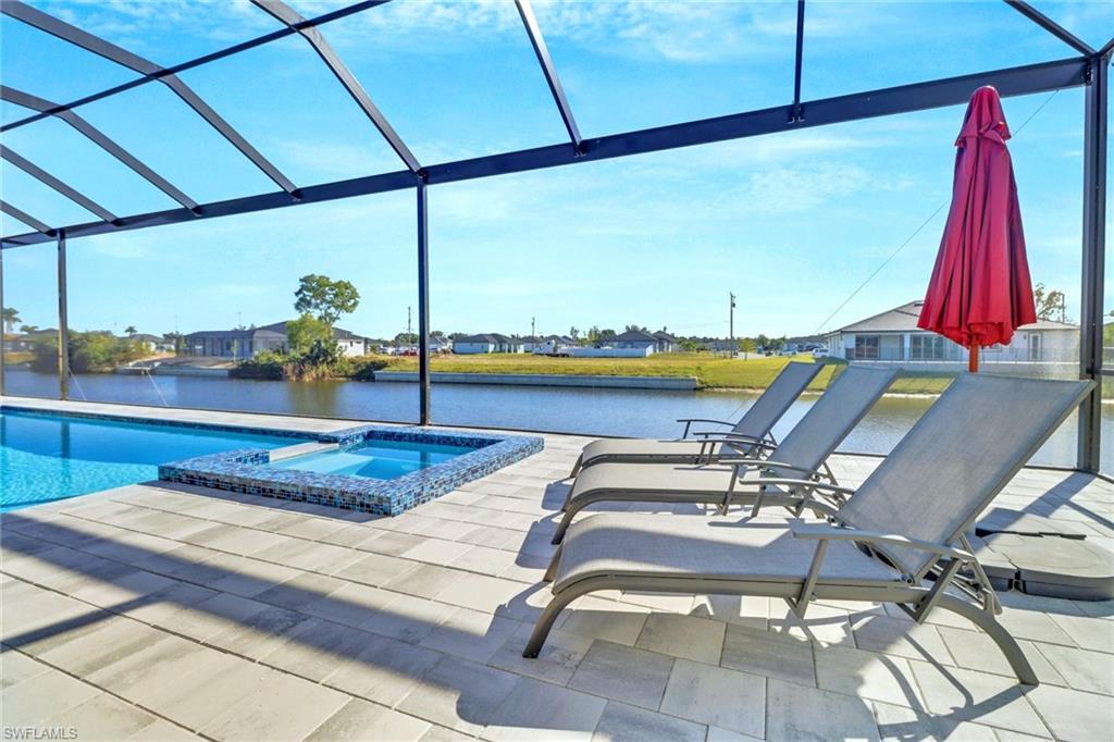 Screened lanai featuring a swimming pool, integrated spa with mosaic tile surround, and expansive paver decking overlooking a waterfront canal