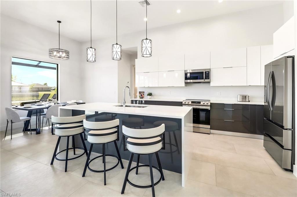 Modern kitchen featuring a large center island with integrated sink, two-tone cabinetry with gloss finishes, stainless steel appliances, and light-toned tile flooring