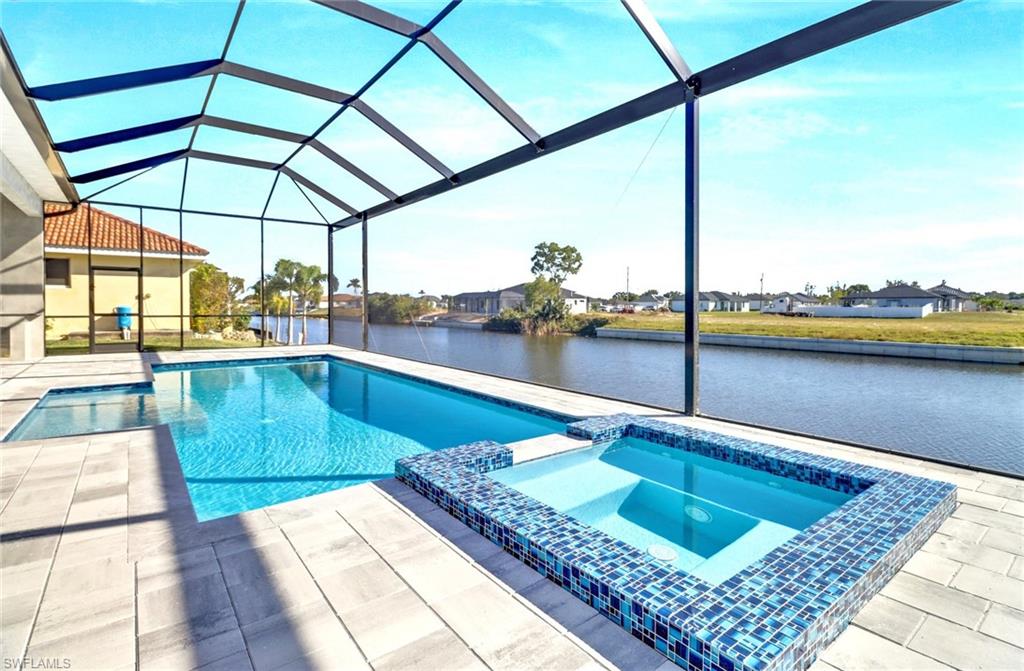 Screened-in outdoor living space featuring a rectangular swimming pool, integrated spa with blue mosaic tile, and concrete paver decking