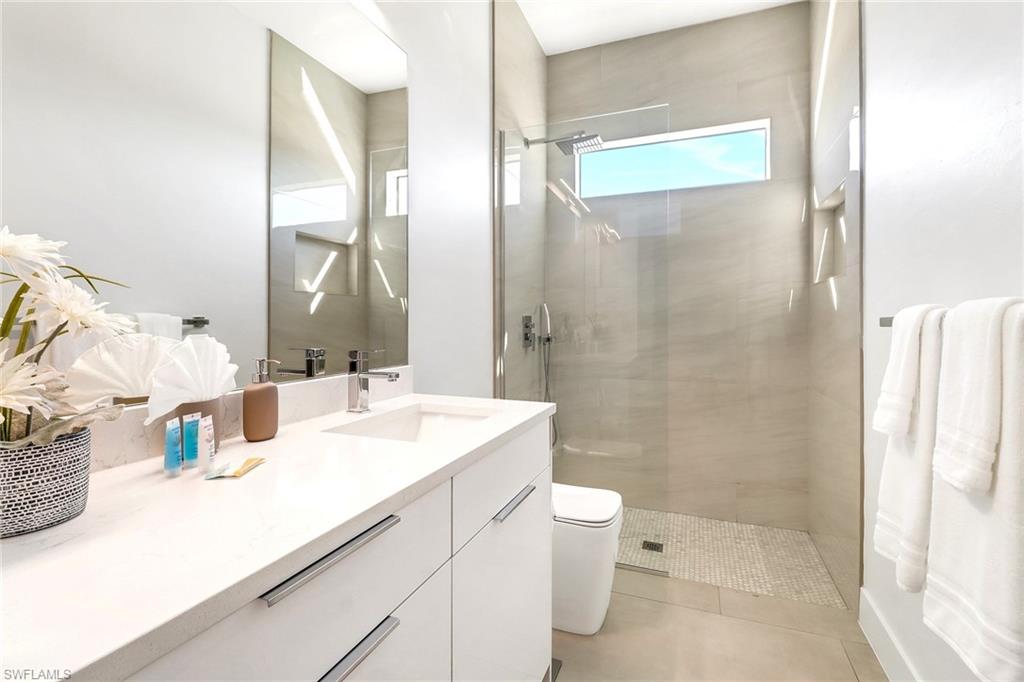 Contemporary bathroom featuring a white vanity with integrated sink, a large wall-mounted mirror, and a glass-enclosed shower with a horizontal window