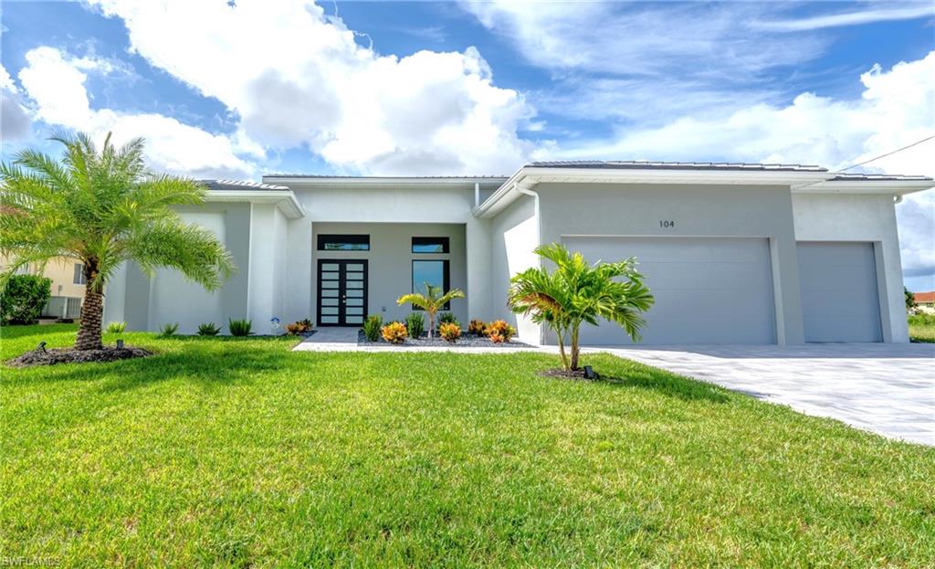 Modern exterior featuring a prominent entry with a double door, two-car garage, manicured lawn, and mature palm trees