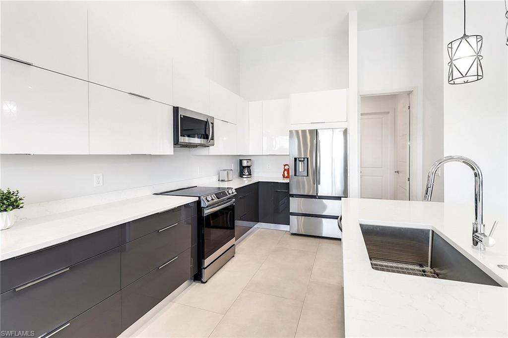 Modern kitchen featuring two-tone cabinetry, stainless steel appliances, a large single-basin sink with a gooseneck faucet, light-colored countertops, and recessed lighting