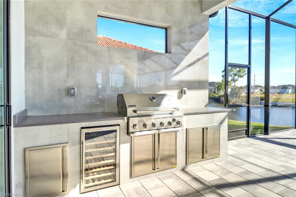 Outdoor kitchen featuring a built-in stainless steel grill, beverage cooler, and integrated storage cabinetry