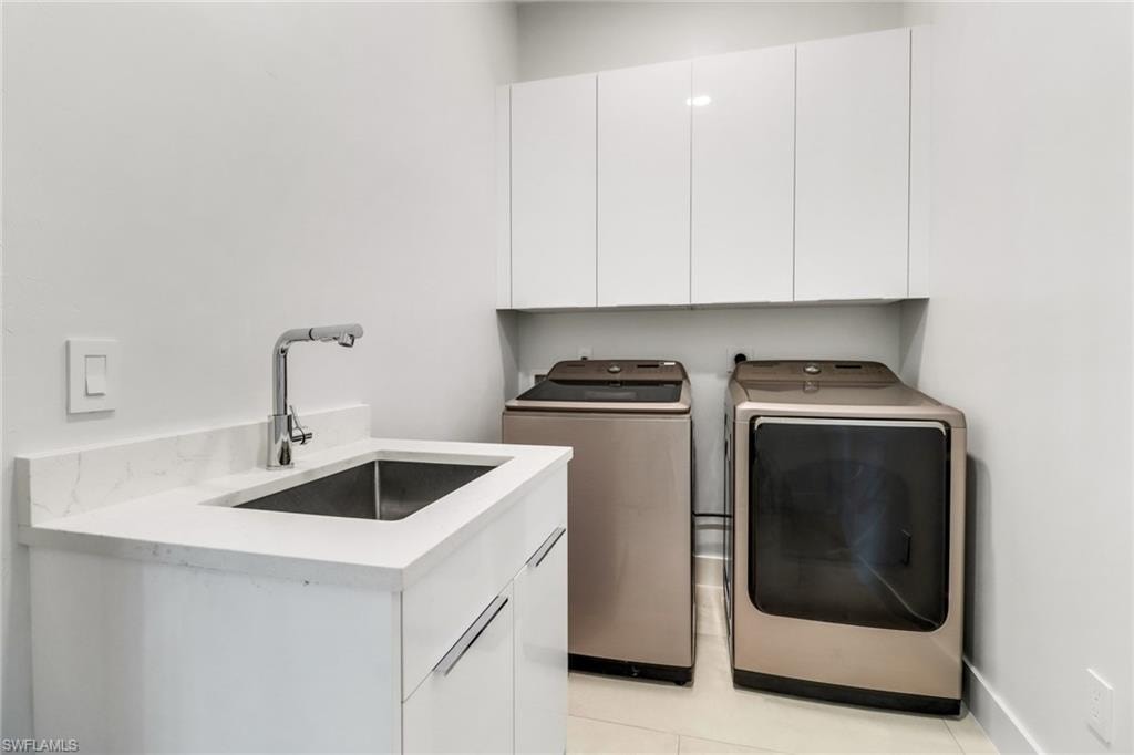 Laundry area featuring a utility sink with a chrome gooseneck faucet, white cabinetry, and a stone-finish countertop