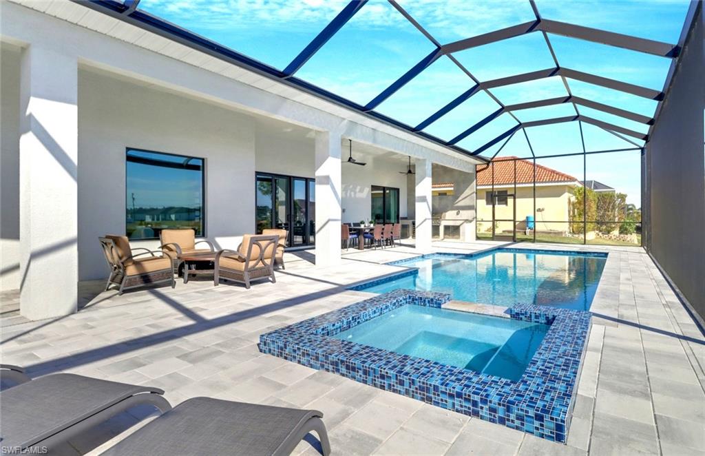 Screened outdoor living area featuring a rectangular pool and integrated spa with blue mosaic tile accents, extensive paver decking, and a covered patio