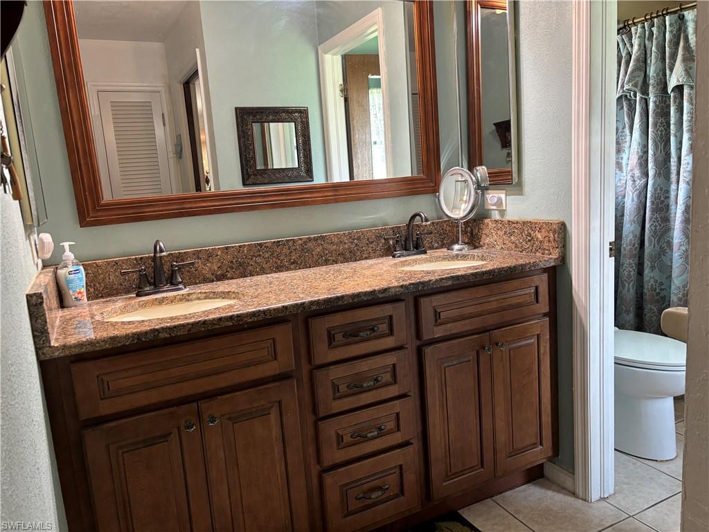 Dual vanity with a stone-finish countertop, wood-finish cabinetry, and oil-rubbed bronze fixtures