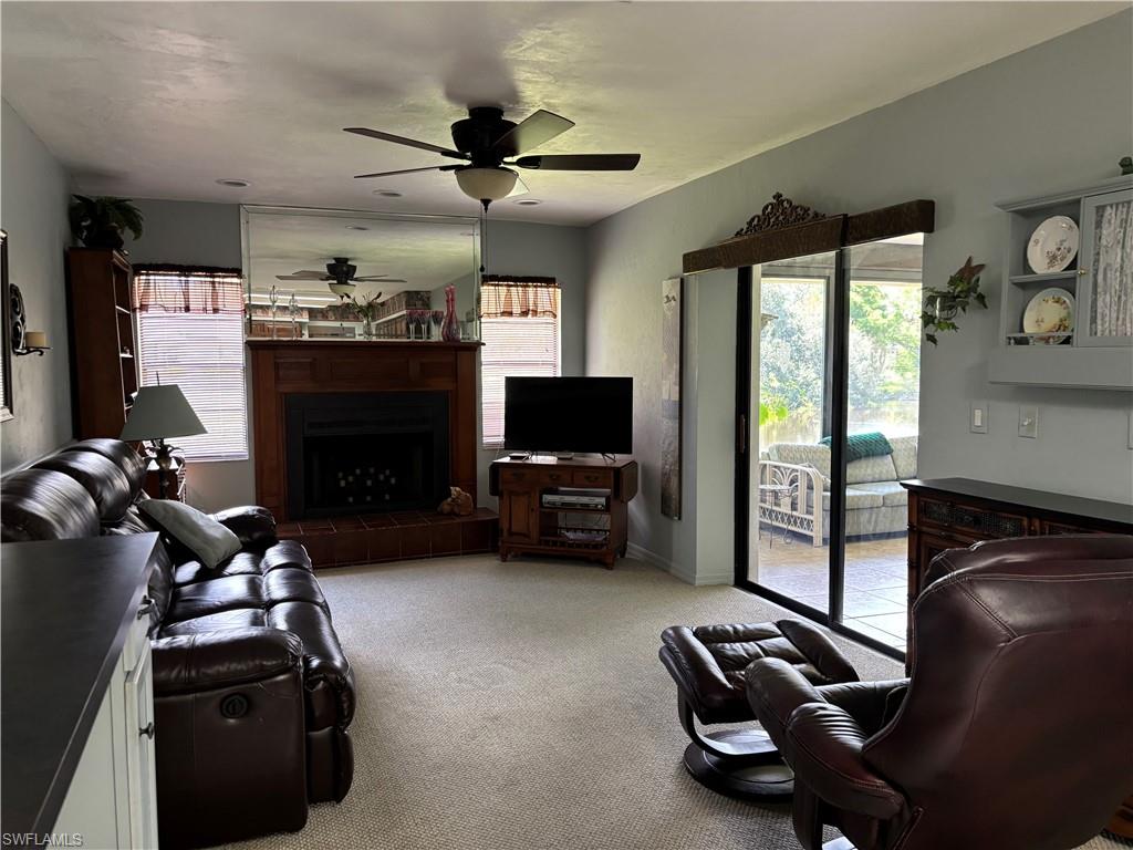 Living area featuring a fireplace with a wood mantle and brick hearth, ceiling fan, and carpet flooring