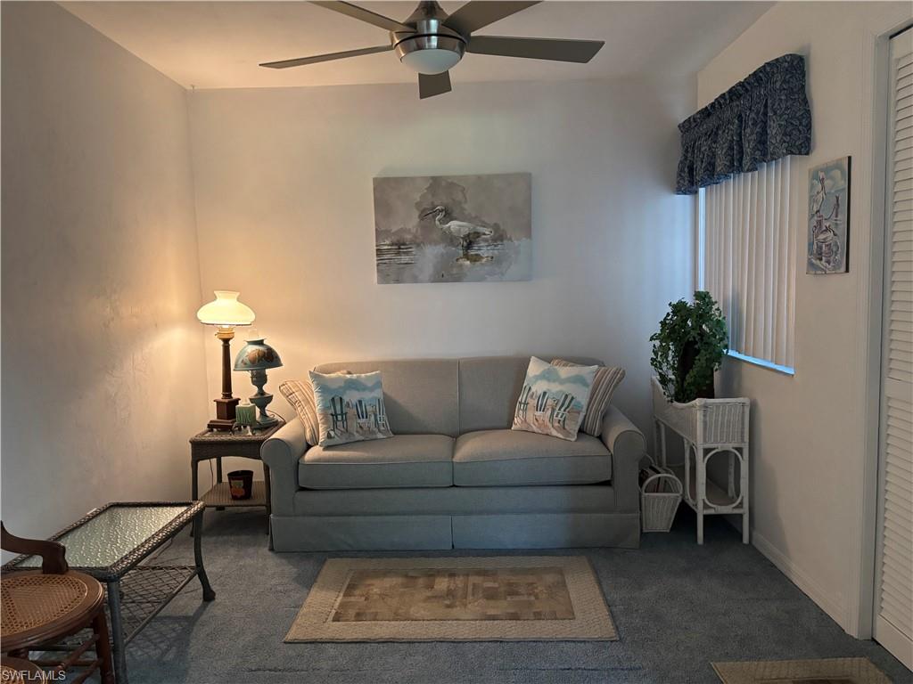 Living area featuring a ceiling fan, wall-to-wall carpeting, and vertical blinds