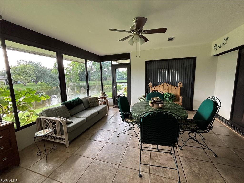 Enclosed sunroom with ample natural light, featuring tiled flooring, a ceiling fan, and expansive window panels overlooking a body of water