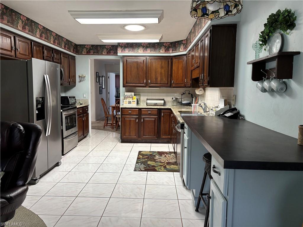 Kitchen featuring wood cabinetry, stainless steel appliances, white tile flooring, and a breakfast bar with dark countertops