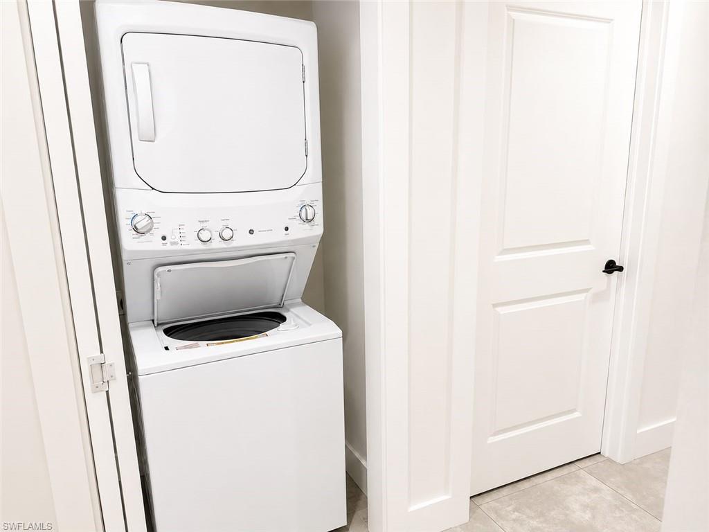 White stackable washer and dryer unit, white paneled doors with black hardware, and light-toned floor tiling