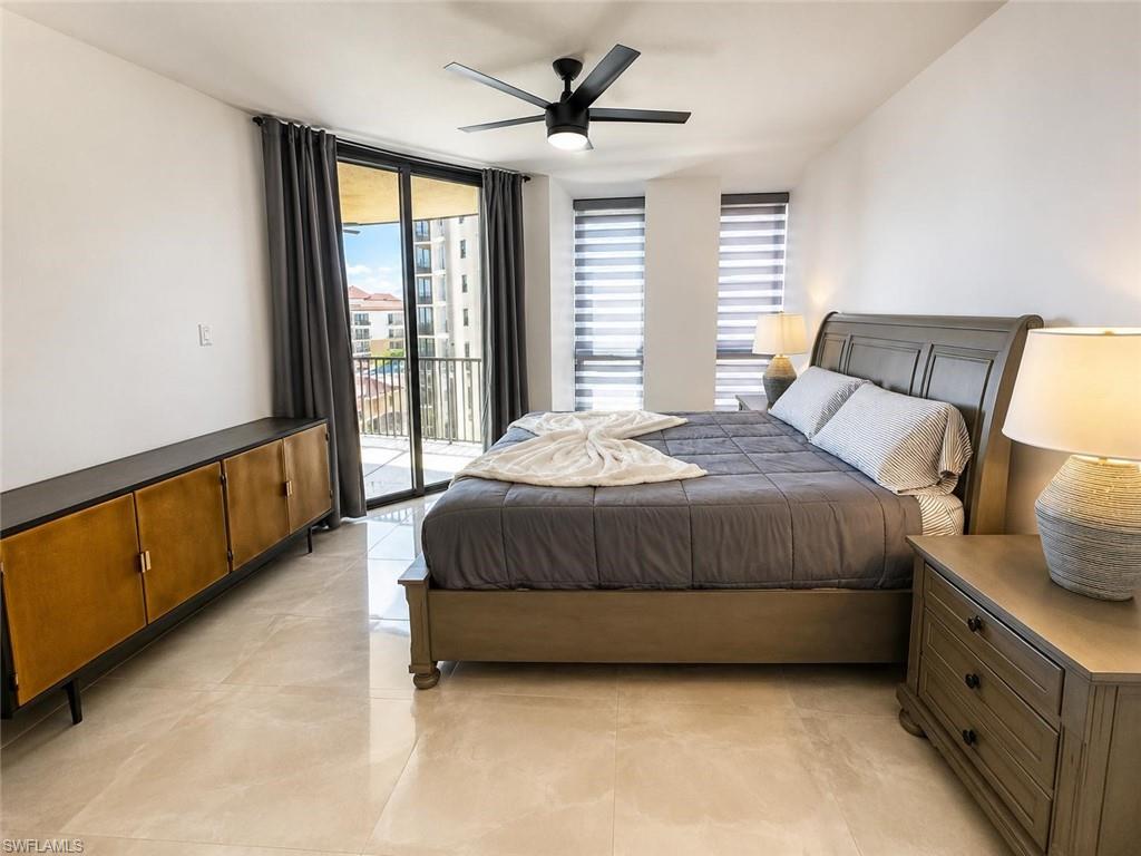 Bright interior space featuring light-toned tile flooring, a dark ceiling fan, a private balcony with a dark railing, and vertical window blinds