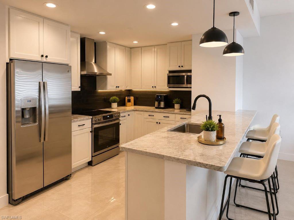 Modern kitchen featuring white shaker cabinetry, stainless steel appliances, a bar-height island with a sink, pendant lighting, and recessed overhead lighting