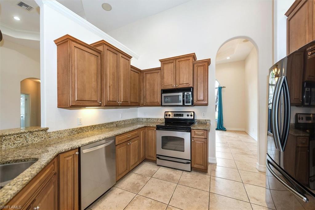 Kitchen featuring appliances with stainless steel finishes, light stone counters, arched walkways, brown cabinets, and recessed lighting
