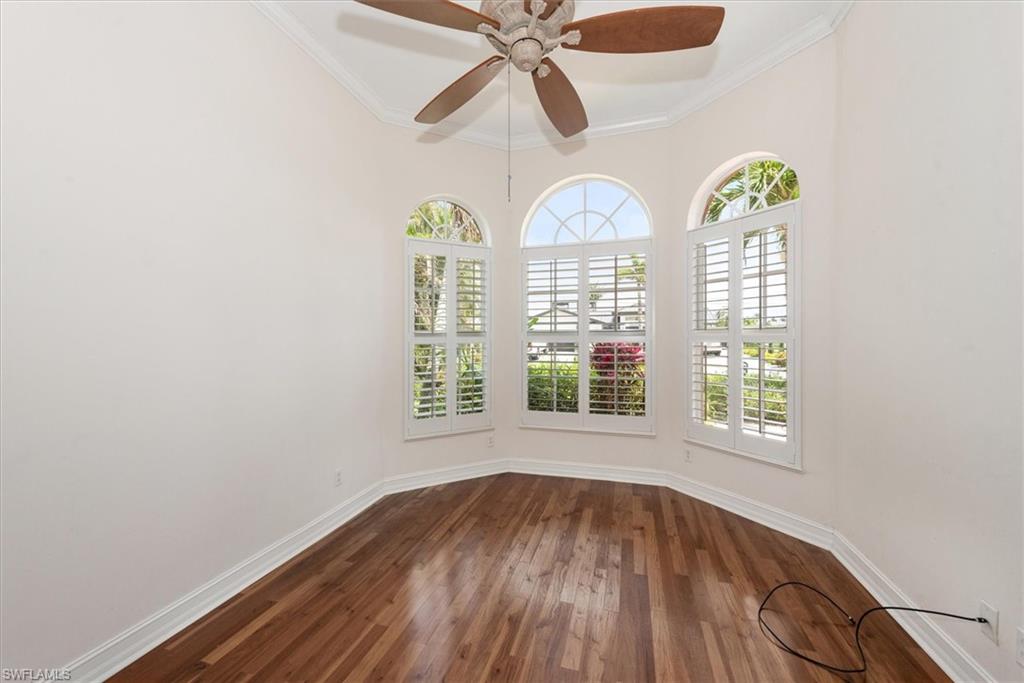 Spare room with dark wood-style flooring, healthy amount of natural light, baseboards, crown molding, and a ceiling fan