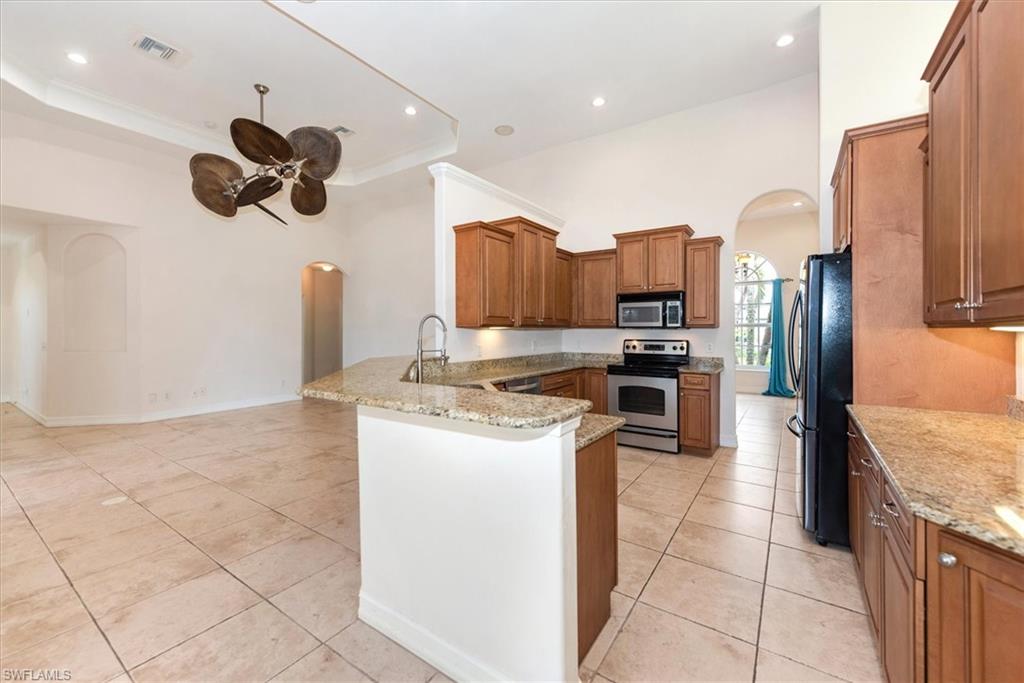 Kitchen with arched walkways, stainless steel appliances, a peninsula, brown cabinets, and light stone counters