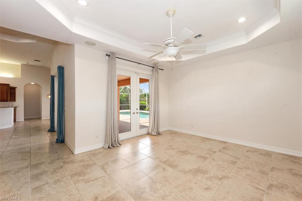 Unfurnished room featuring a raised ceiling, arched walkways, a ceiling fan, crown molding, and baseboards