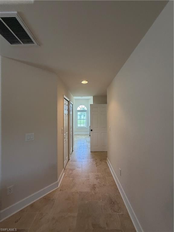 Travertine flooring extends through this hallway, into walk-in closet, bathroom entry featuring crisp white baseboards and neutral wall tones