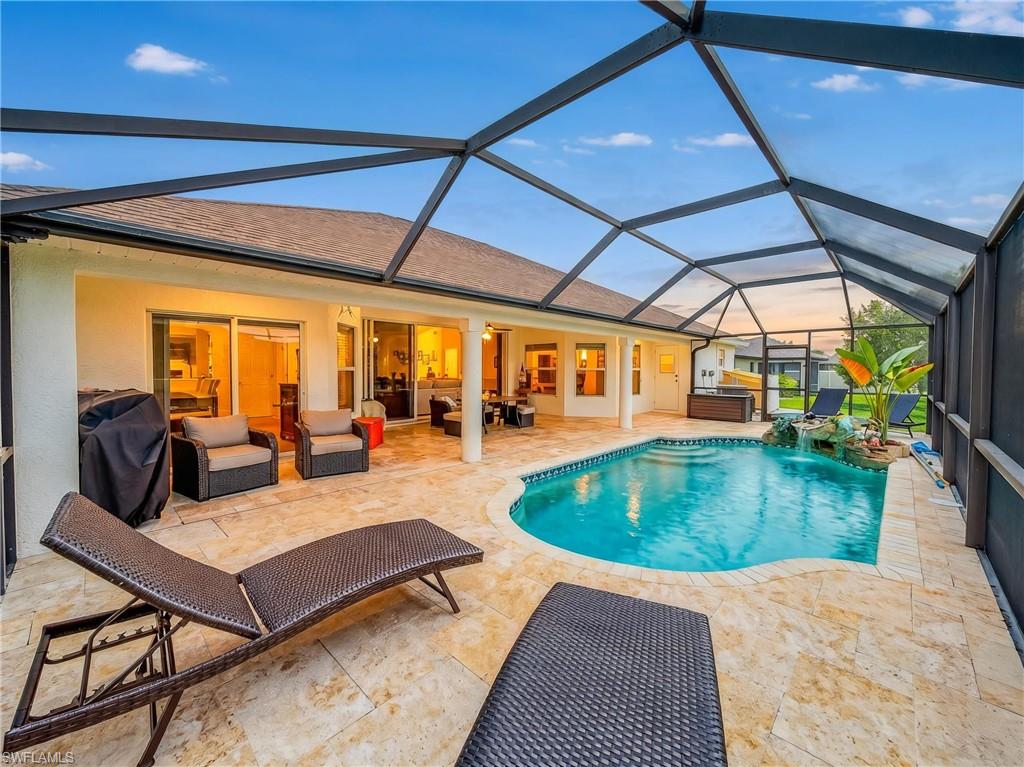 Screened pool enclosure featuring a freeform swimming pool, integrated spa, and expansive travertine tile patio