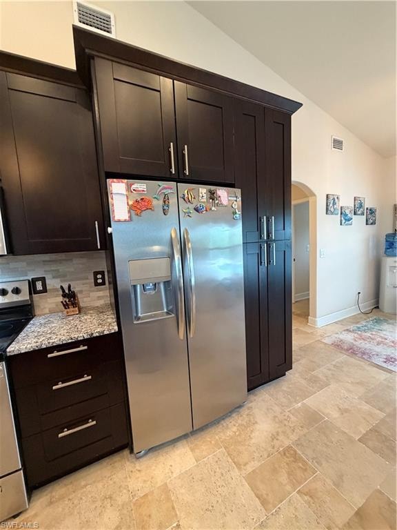 Kitchen featuring rich dark wood cabinetry with crown molding, stainless steel refrigerator, light granite countertops, and a neutral tile backsplash