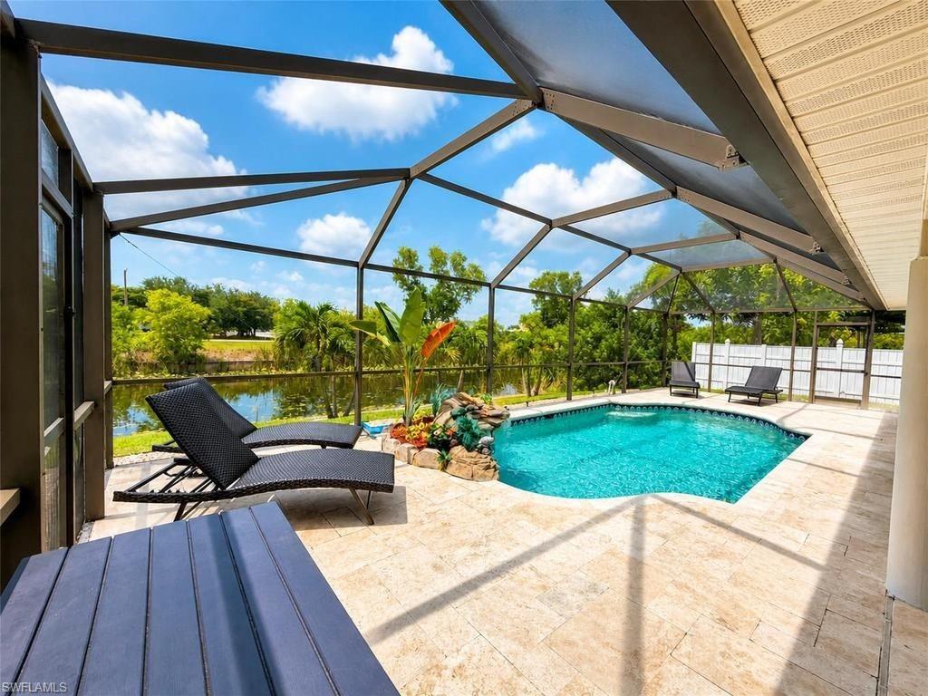 Screened enclosure featuring a contoured pool, a decorative rock waterfall, and a tiled patio