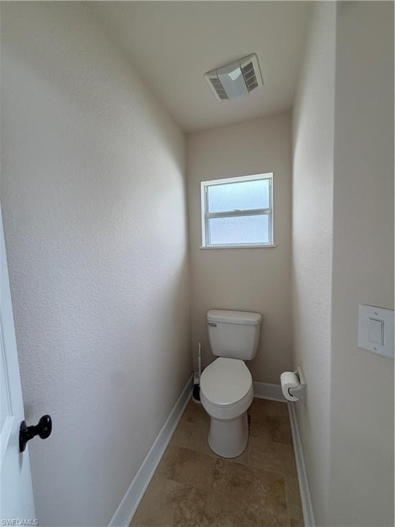 Compact powder room featuring a window, ceiling-mounted exhaust fan, tiled flooring, travertine tiles, white baseboards, and a white toilet