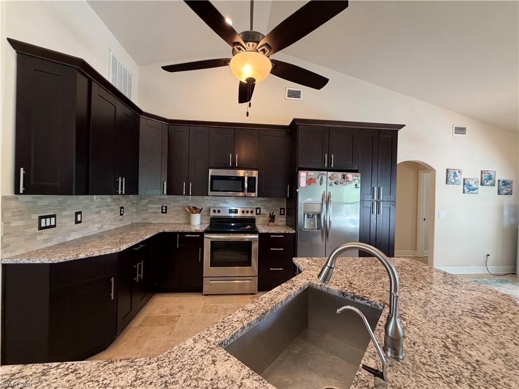 Kitchen featuring dark wood cabinetry with crown molding, stainless steel appliances, granite countertops, and a tile backsplash