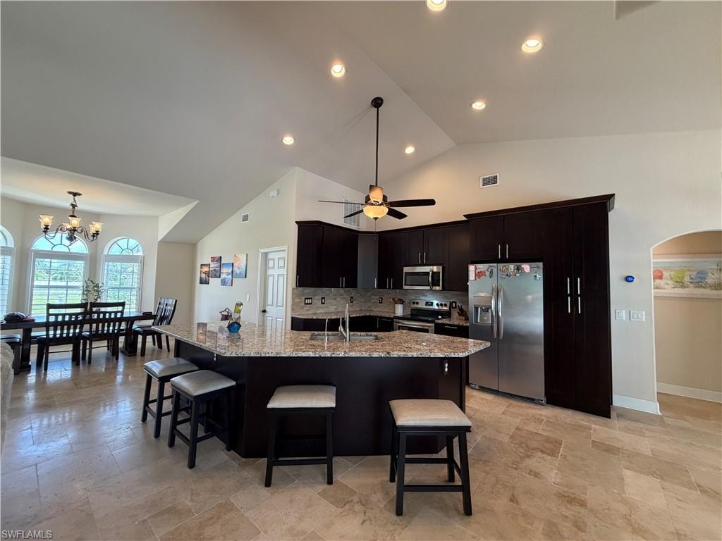 Open-concept kitchen featuring dark wood cabinetry, stainless steel appliances, granite countertops, and a breakfast bar