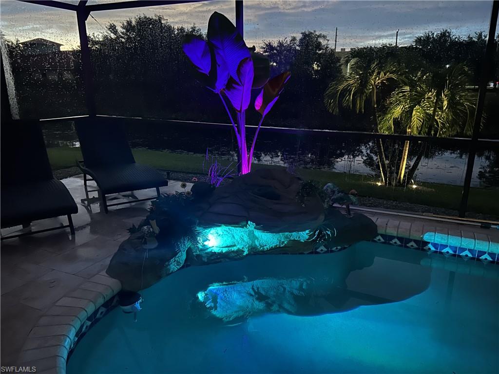 Screened lanai featuring a swimming pool with integrated rock features and colorful accent lighting