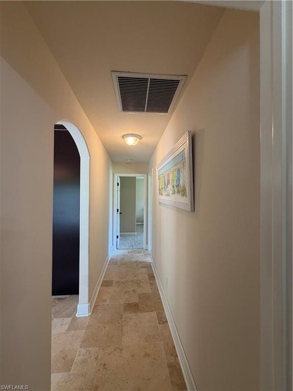 Hallway featuring neutral-toned walls, travertine tile flooring, and white baseboards