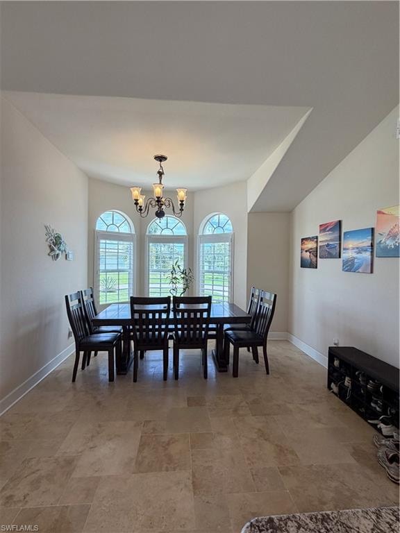 Dining area featuring arched windows with white plantation shutters, a bronze chandelier, and large format stone tile flooring