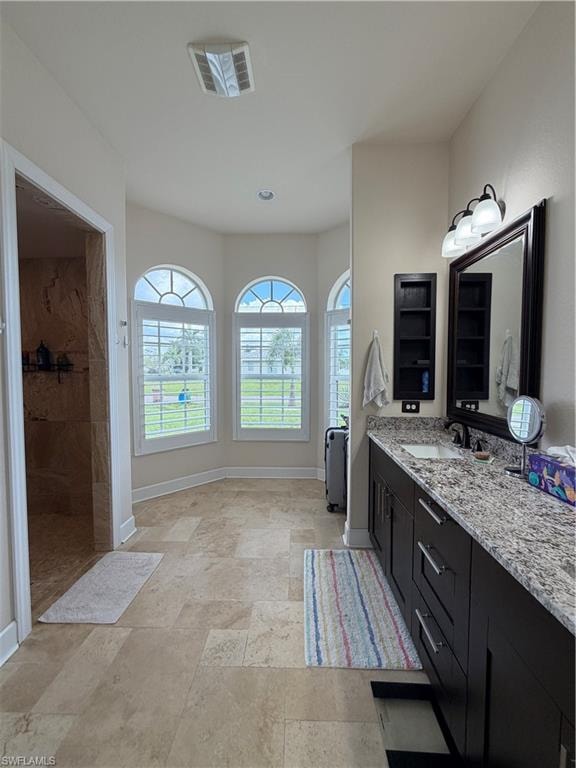 Primary Bathroom featuring a dual vanity with a granite countertops, a large framed mirror, and three arched windows with plantation shutters