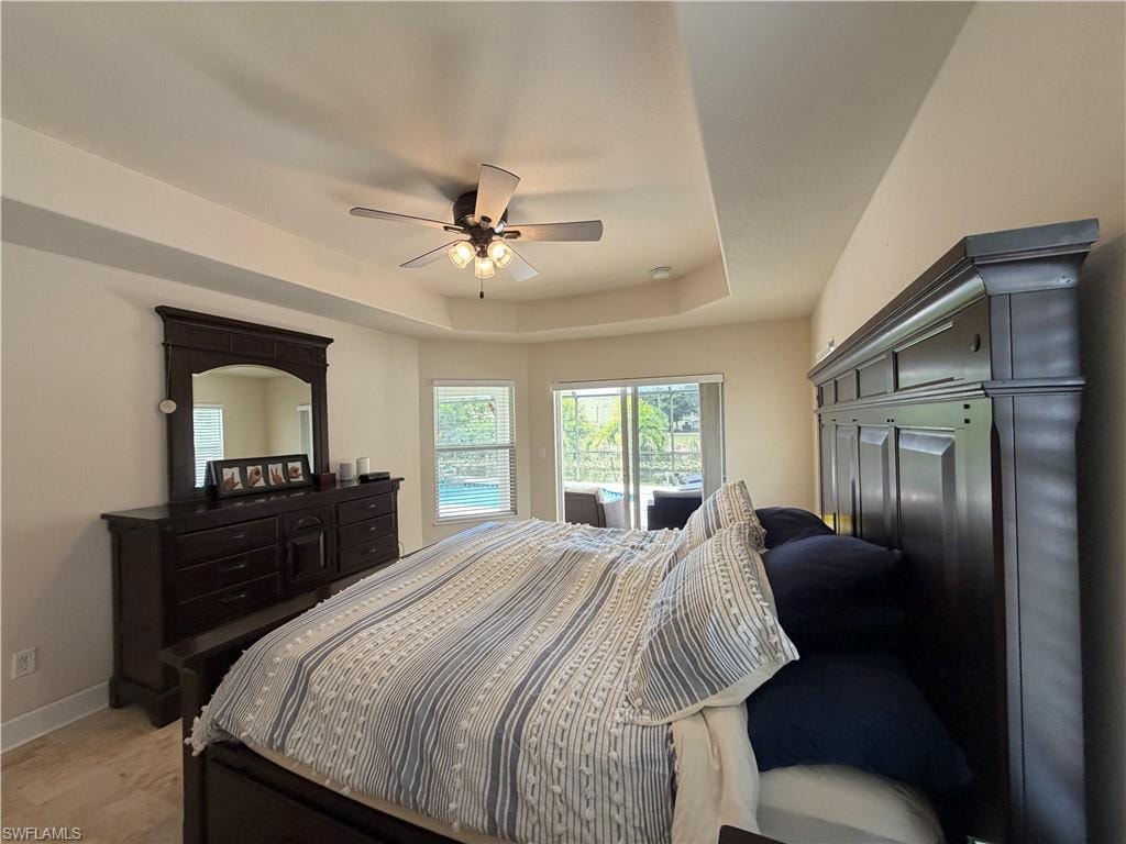 Primary Bedroom Tray ceiling with a ceiling fan, light wood-finish flooring, and multiple windows overlooking a screened lanai with a pool