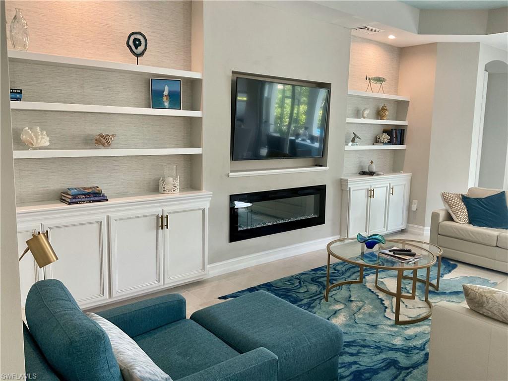Living room with a glass covered fireplace, built in shelves, baseboards, light tile patterned floors, and recessed lighting