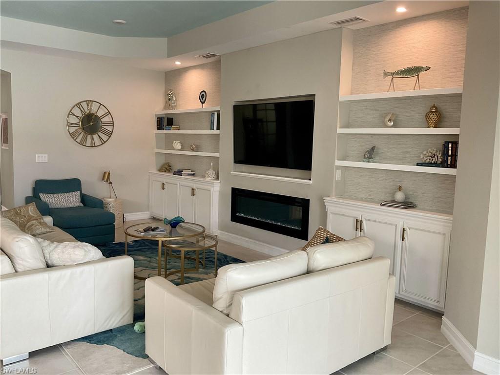 Living room featuring light tile patterned flooring, a glass covered fireplace, built in shelves, recessed lighting, and baseboards