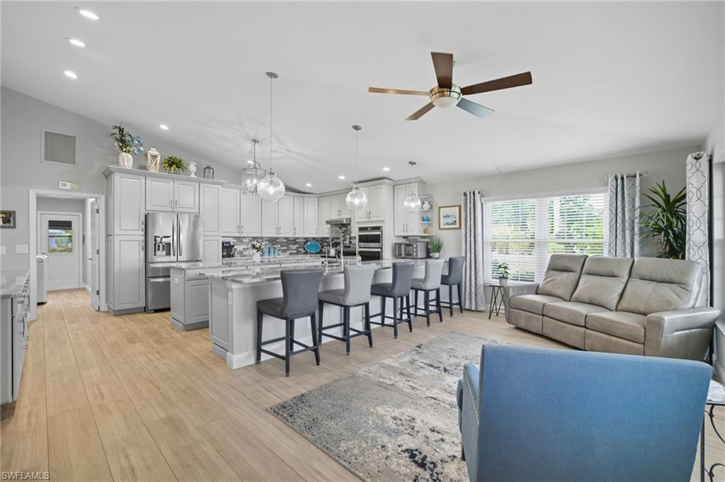 Open-concept kitchen and living area featuring high vaulted ceilings, light wood-finish flooring, a kitchen island with seating, a built-in oven, and pendant lighting