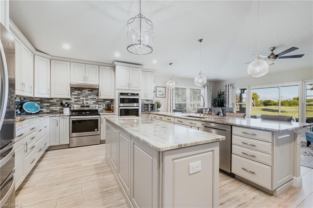Spacious kitchen featuring an expansive center island, light wood-finish flooring, white cabinetry, stainless steel appliances, and large sliding glass doors overlooking outdoor greenspace
