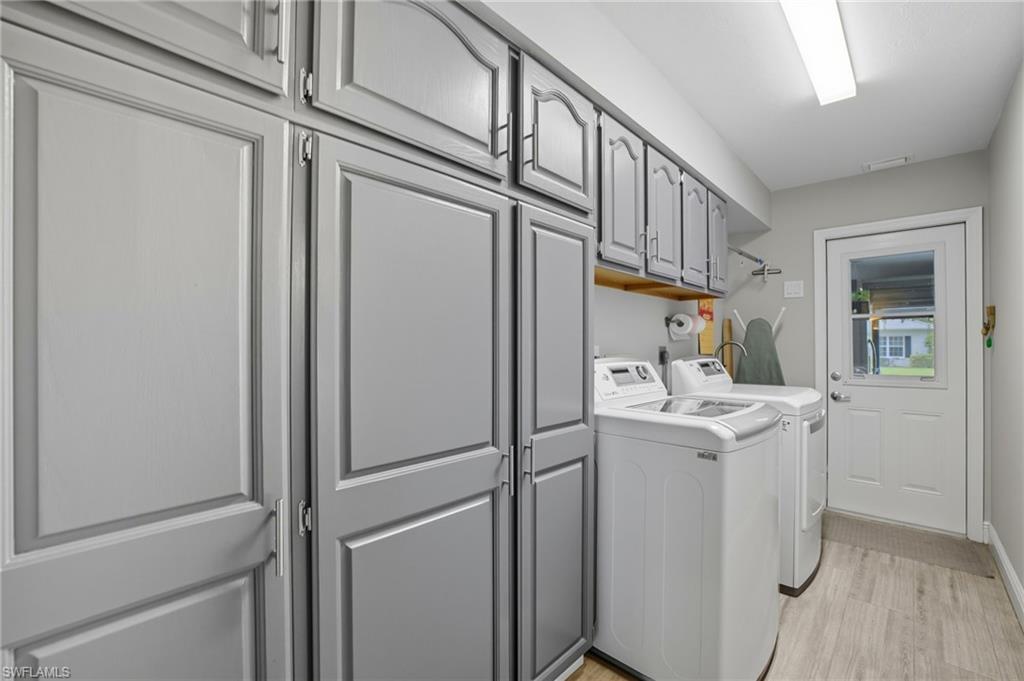 Utility room featuring extensive gray paneled cabinetry providing ample storage, wood-finish flooring, and a white exterior door with clear glass paneling